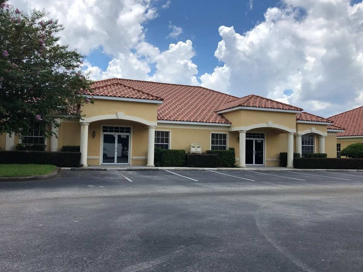 Yellow stucco storefronts with red tile roofs and a parking lot under a partly cloudy sky
