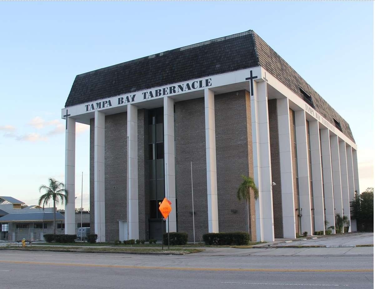 A tall white-columned building with a dark roof and an orange sign near the entrance.