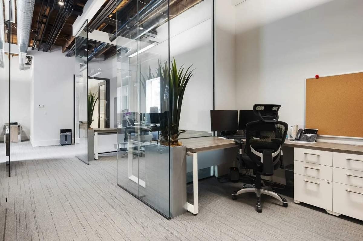 Modern office with glass partitions, desks, black chair, and white cabinets in a bright workspace