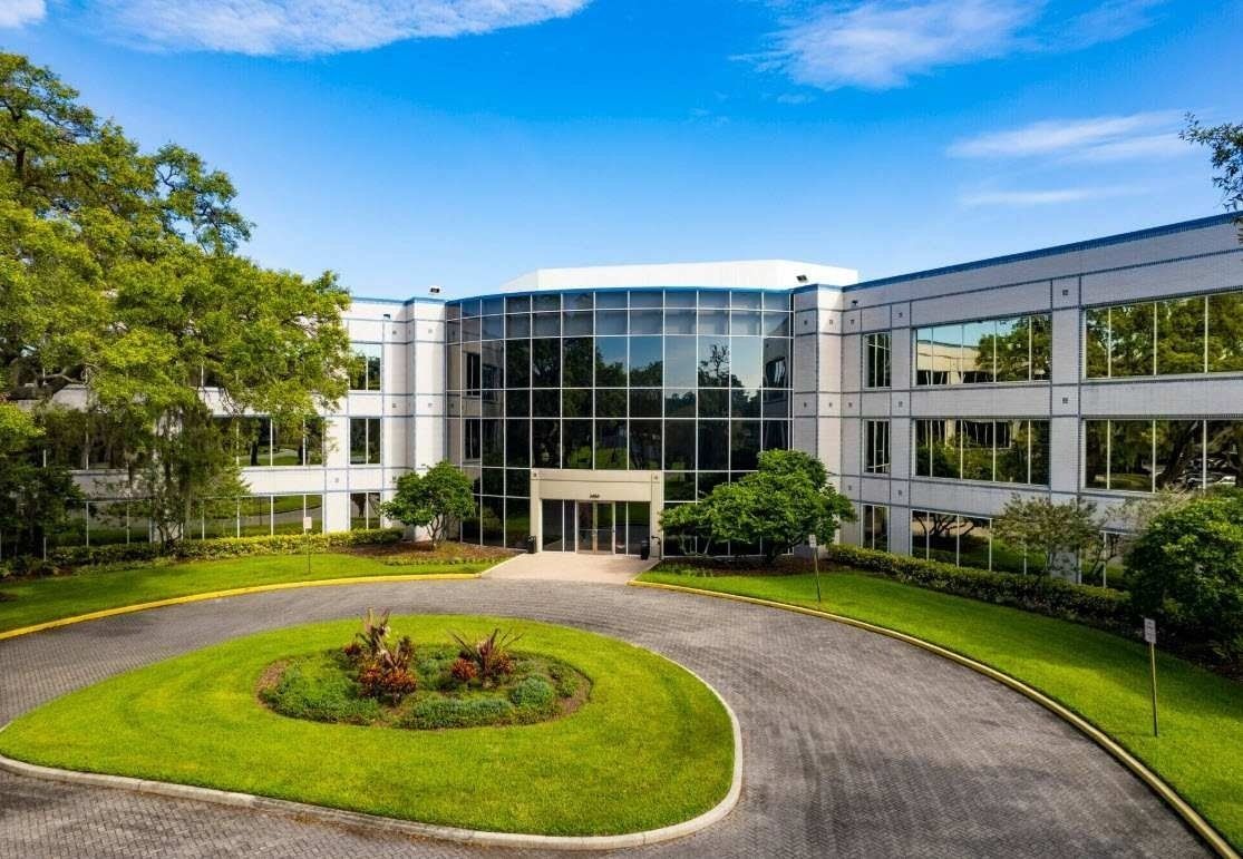 Modern glass office building with landscaped roundabout and green lawn under a blue sky