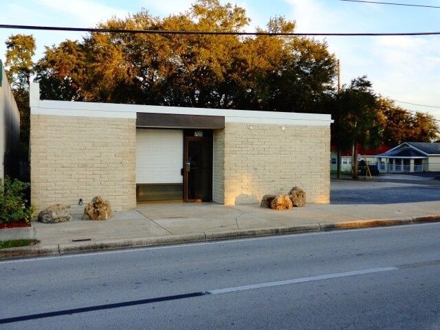 Small beige brick building with a recessed doorway and a sidewalk along a quiet street at sunset