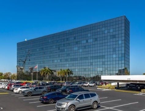 Glass office building with parked cars in a lot on a sunny day
