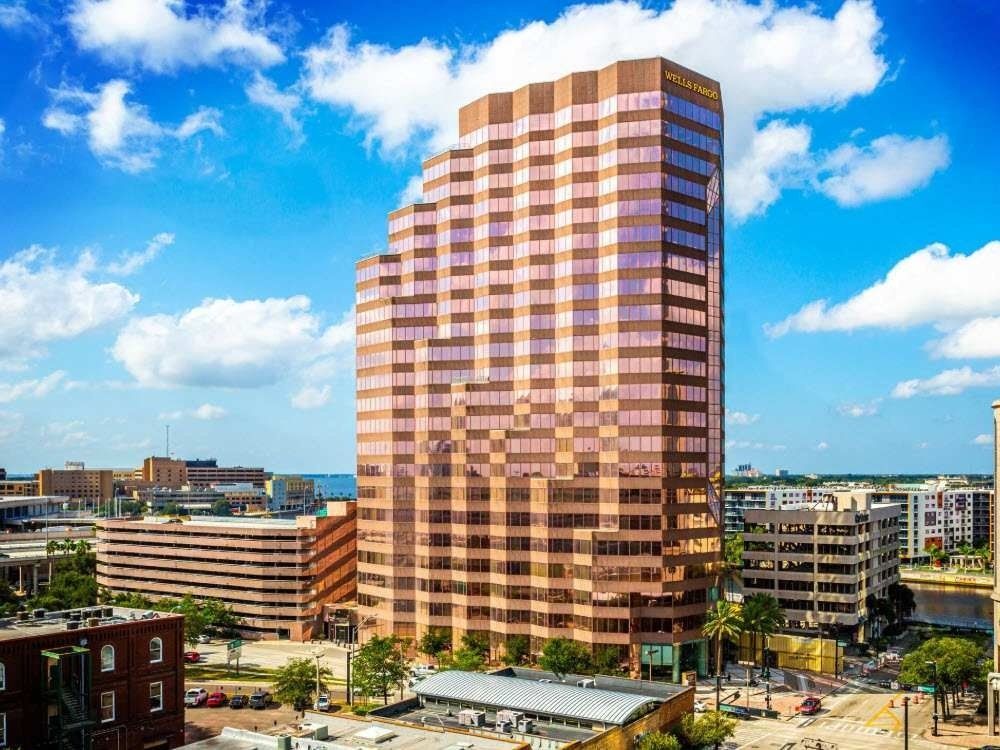 Tall copper-glass high-rise in a sunny city skyline with blue sky and clouds