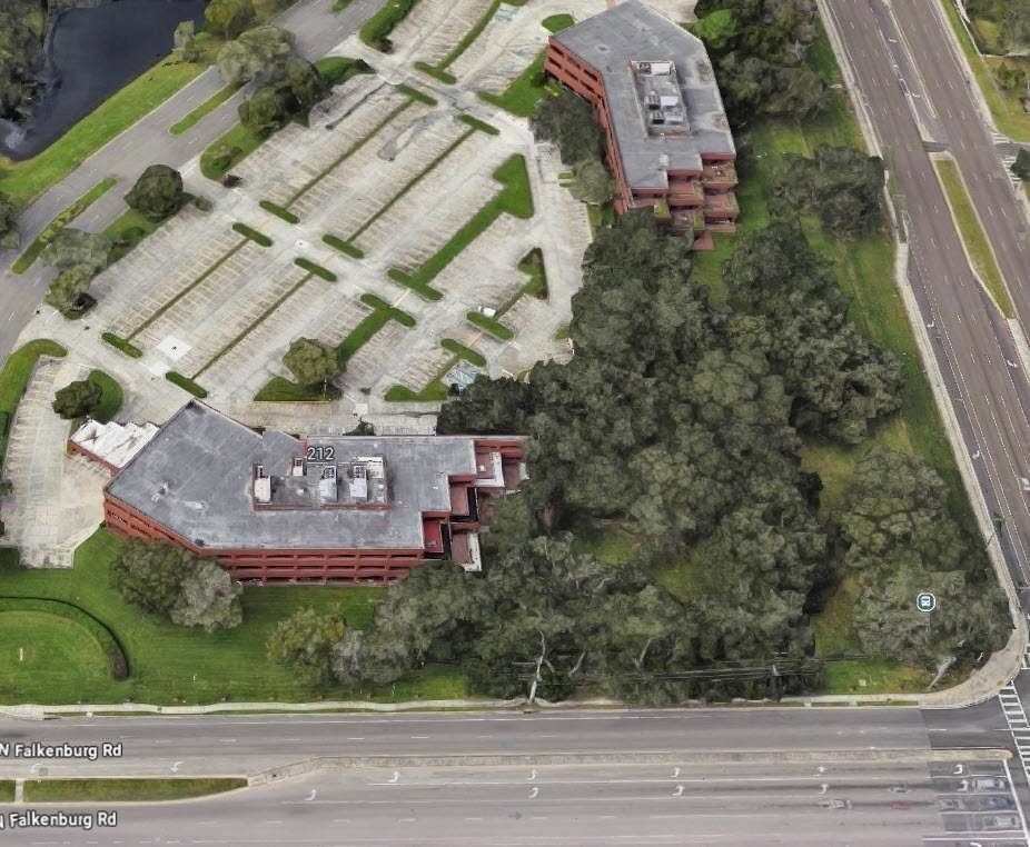 Aerial view of abandoned buildings beside a road, surrounded by trees and empty parking lots