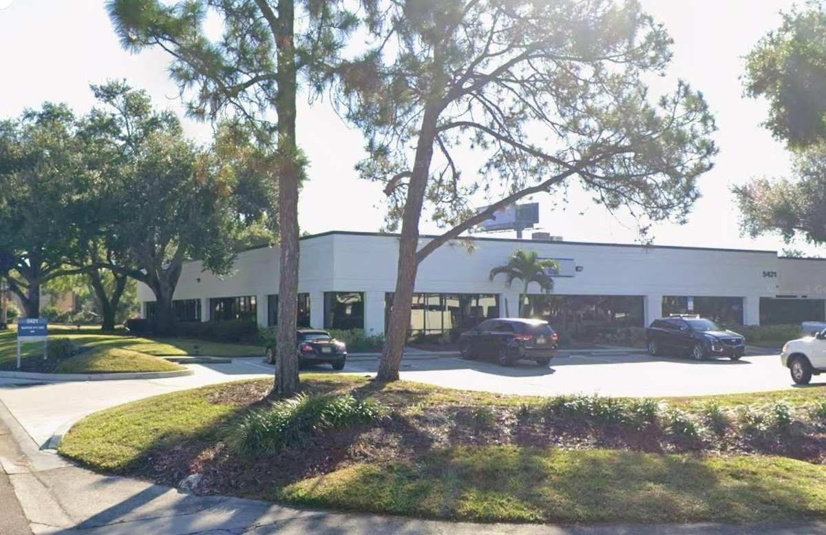 Single-story office building with parked cars and trees in front under bright sunlight
