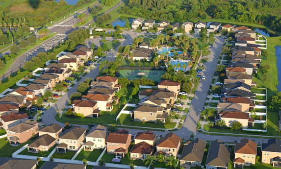 Aerial view of a suburban neighborhood with houses, streets, and a central recreation area with a pool.