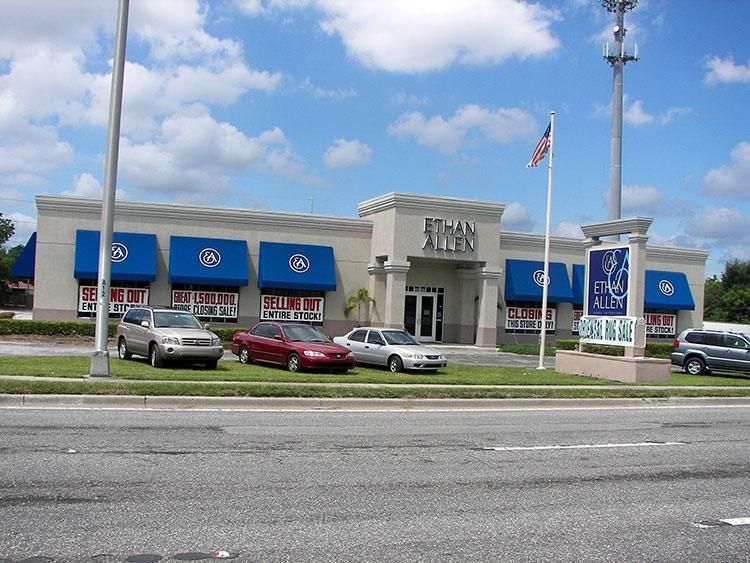 Volkswagen dealership with blue awnings, parked cars, and an American flag by the road