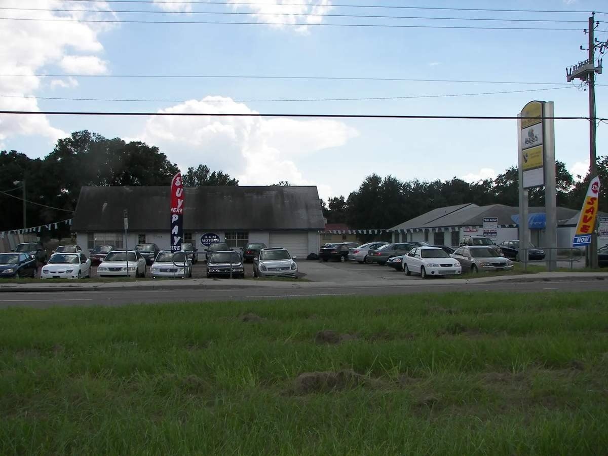 Parking lot of a car dealership with many cars, cloudy sky, and a grassy foreground