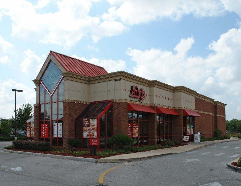 Arby's restaurant building with red roof, tan walls, and brick exterior under a blue, cloudy sky.
