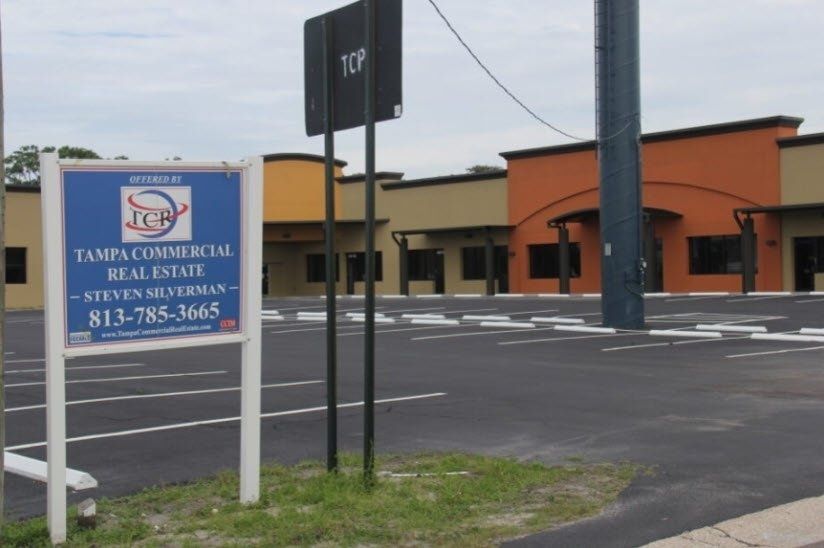 Vacant commercial building with a Tampa Commercial Real Estate sign in front of a parking lot