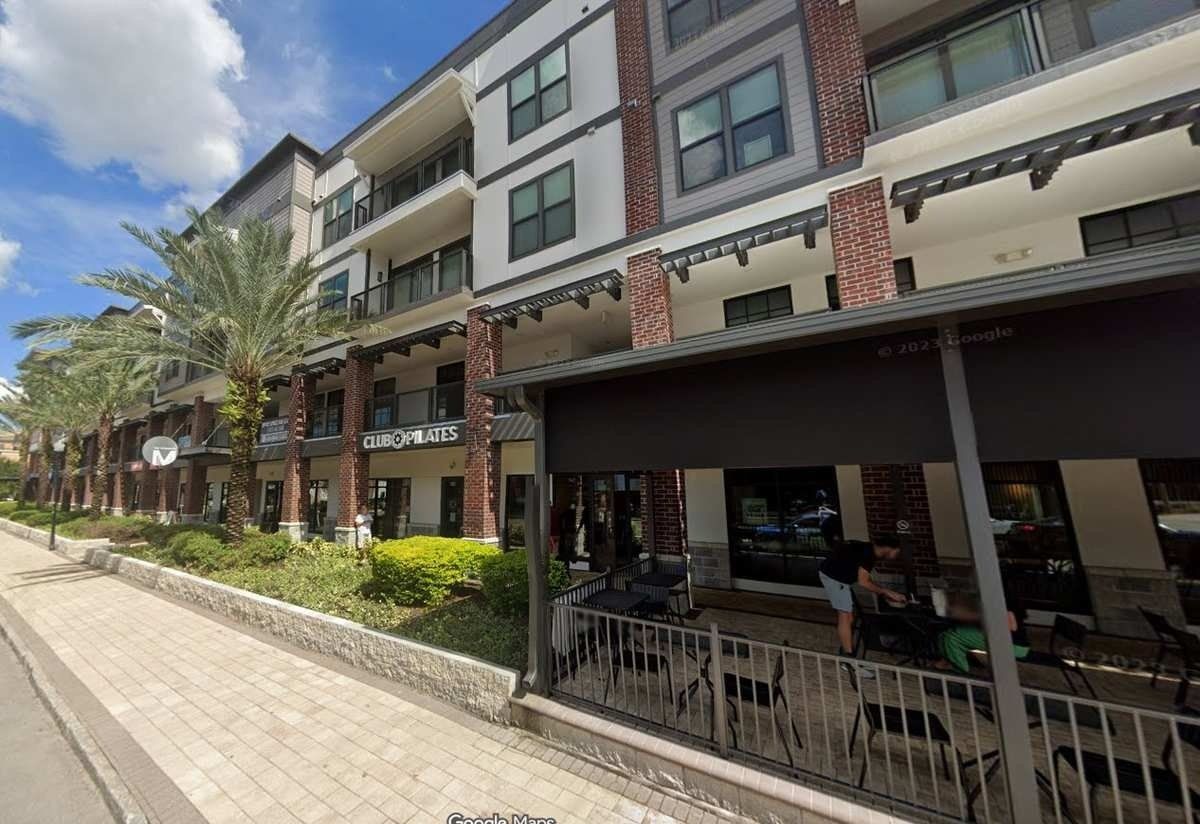 Modern apartment building with balconies, a sidewalk, and outdoor cafe seating on a sunny street