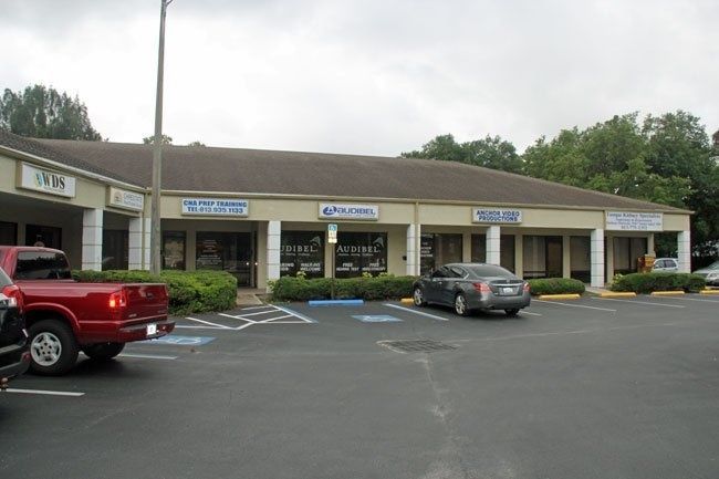 Strip mall storefronts with parked cars in a small shopping center parking lot.