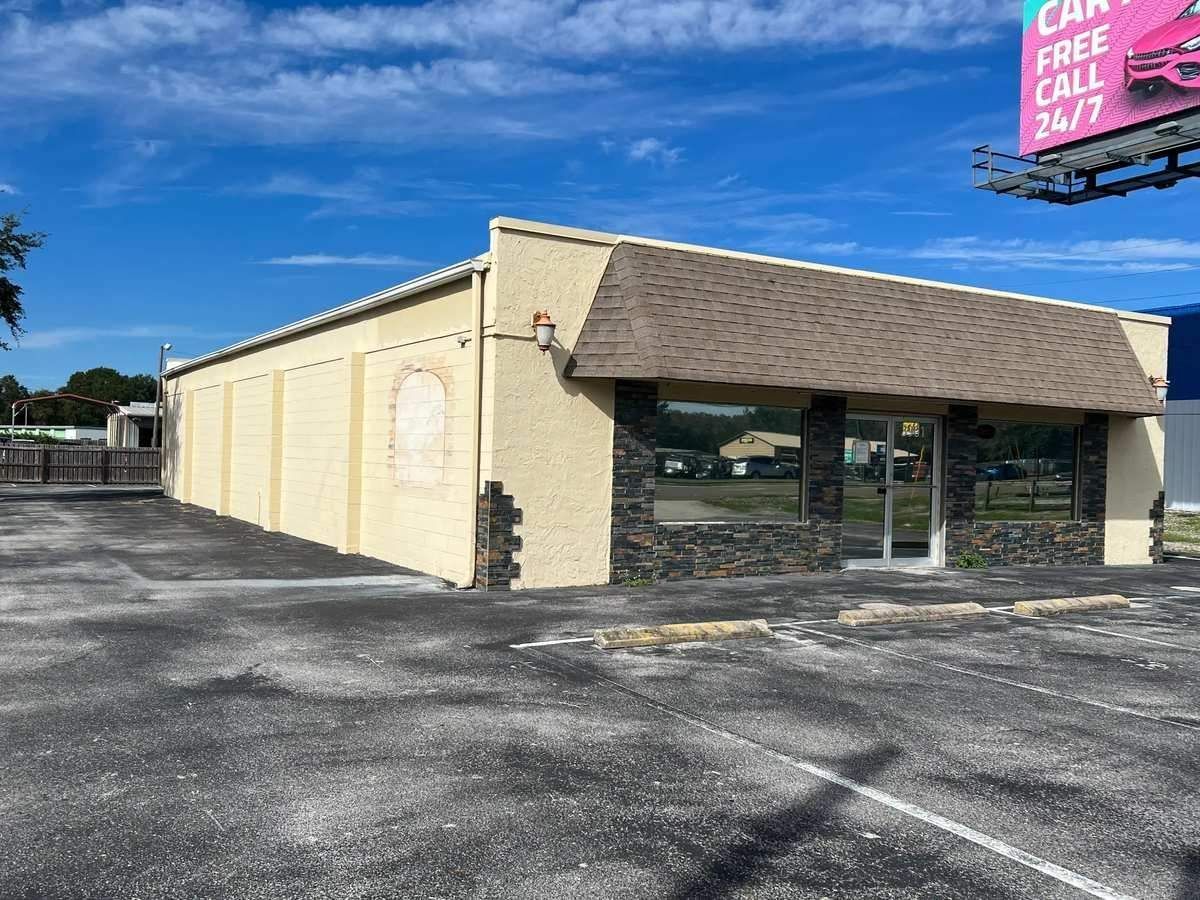 Beige commercial building with tan roof and large windows on an empty asphalt lot under a blue sky