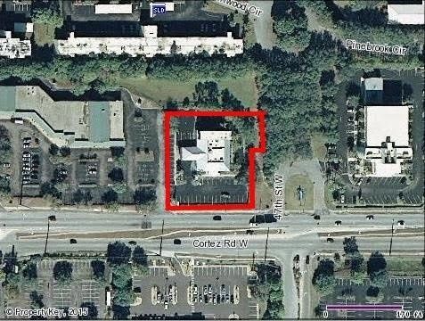 Aerial view of buildings and parking lots, with a central building outlined in red near a road.