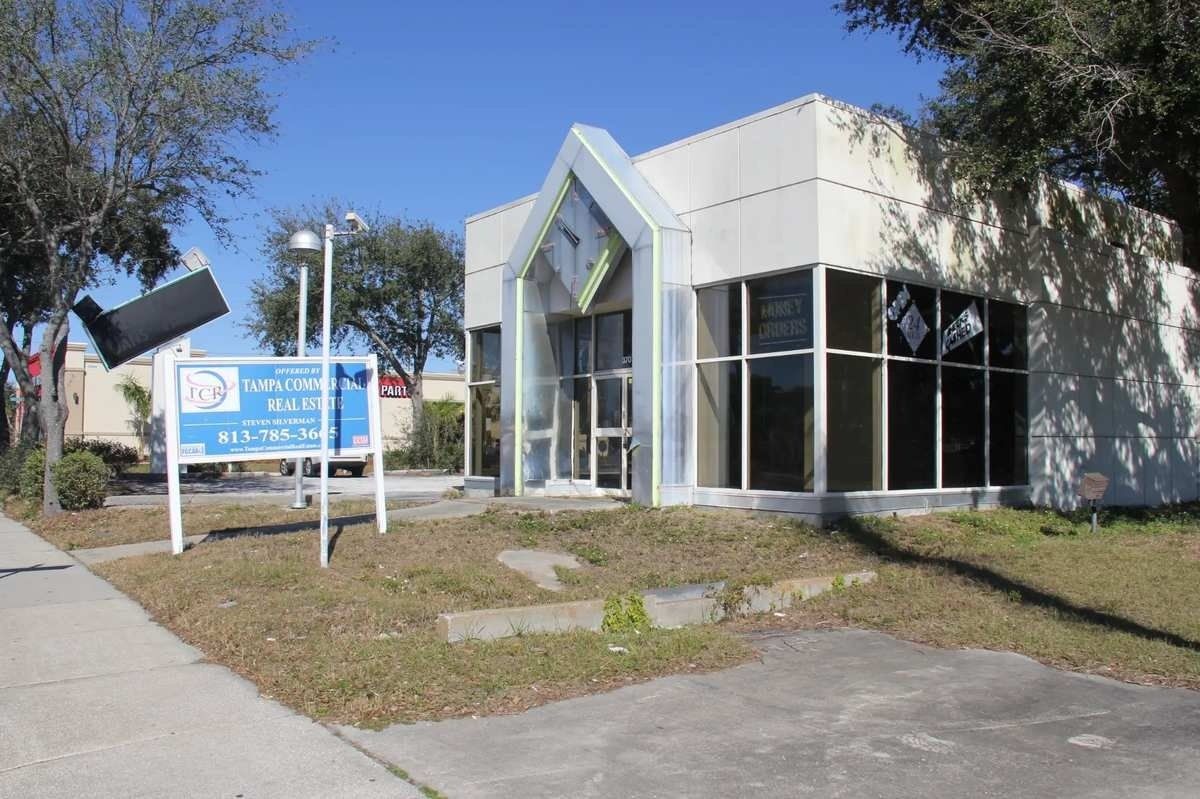 Modern white building with a blue sign and glass entrance beside a sidewalk on a sunny day