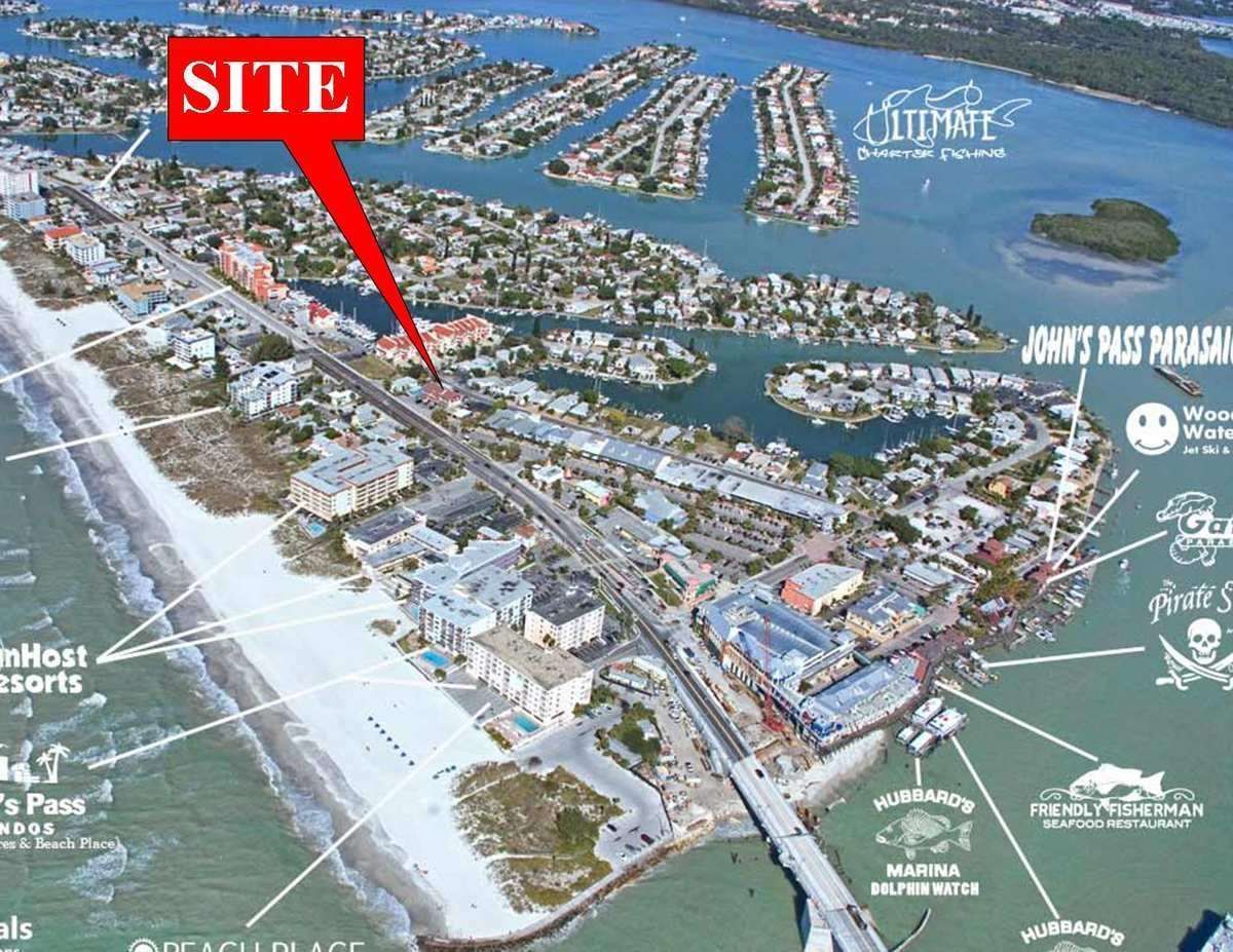 Aerial view of a coastal marina with a red “SITE” label pointing to a street near the waterfront.