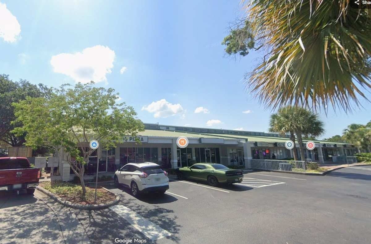 Strip-mall storefronts with parked cars and palm trees on a sunny day