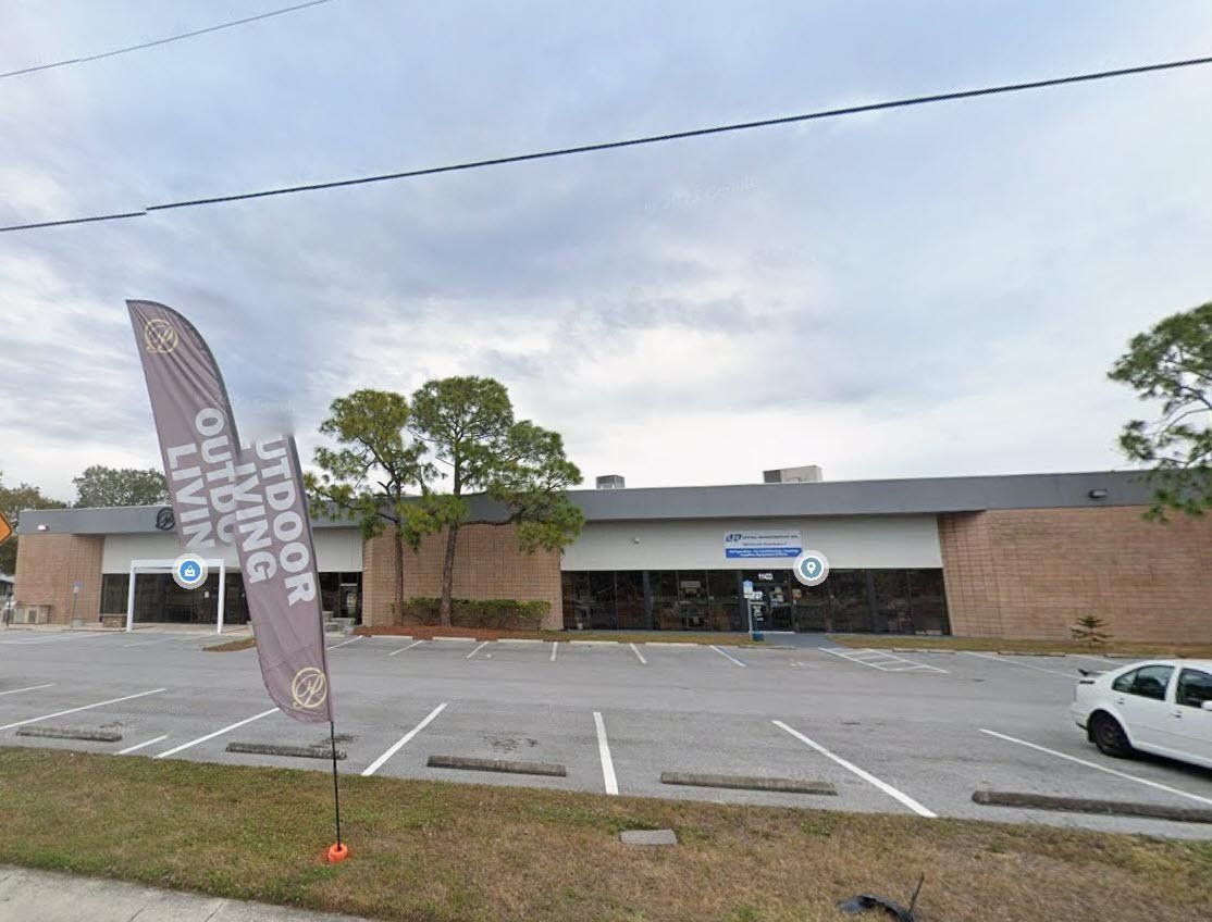 Empty parking lot in front of a brick storefront, with a tall banner and a white car on the right.
