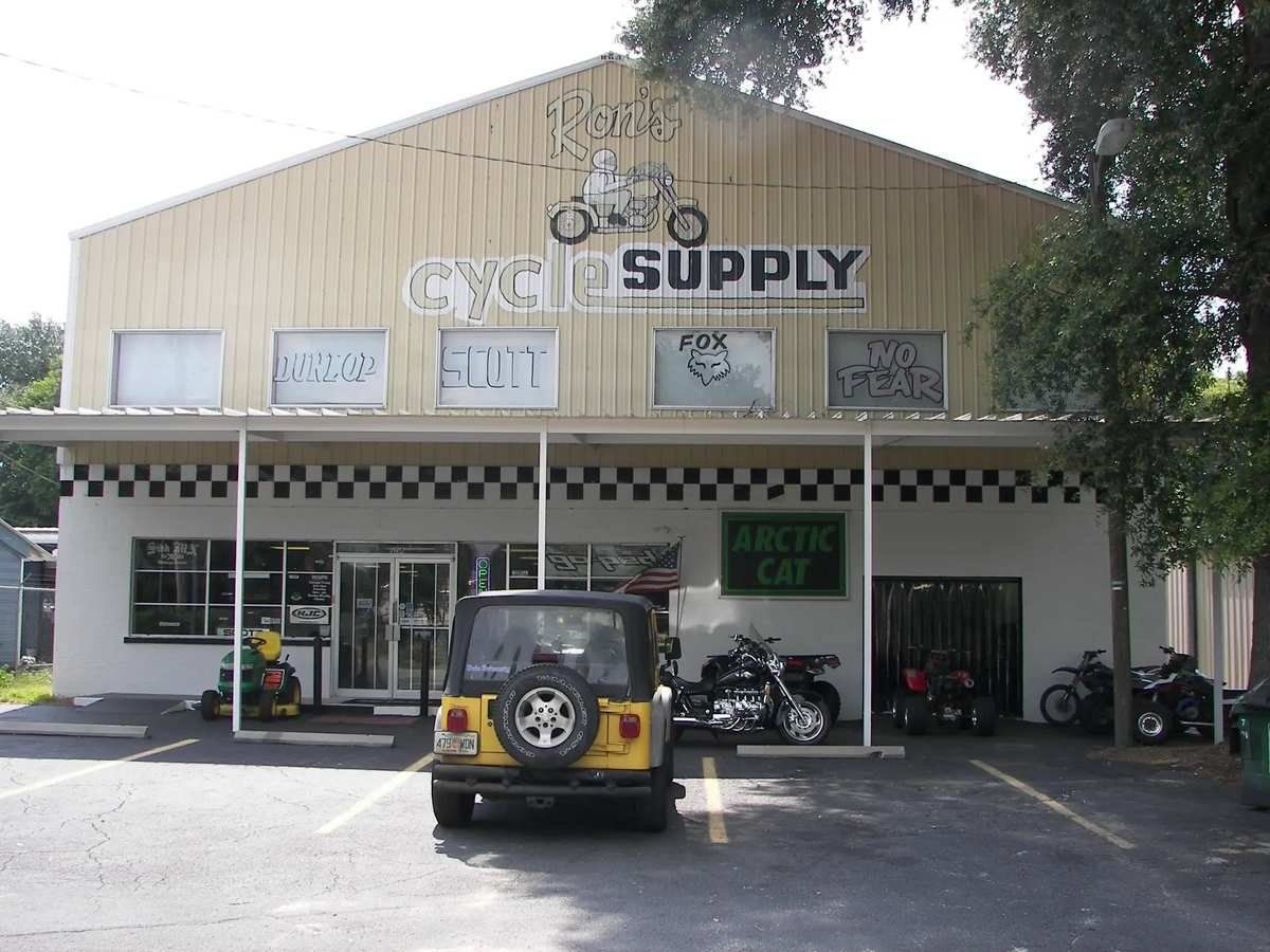 Tan storefront with “SUPPLY” sign, parked jeep and motorcycles under a covered entrance.