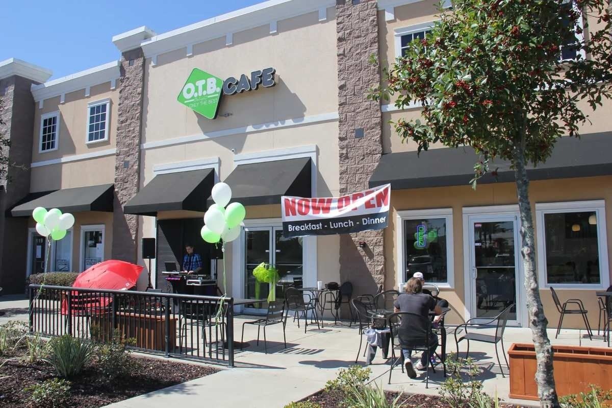 Outdoor cafe storefront with tables, red umbrellas, and green balloons on a sunny day