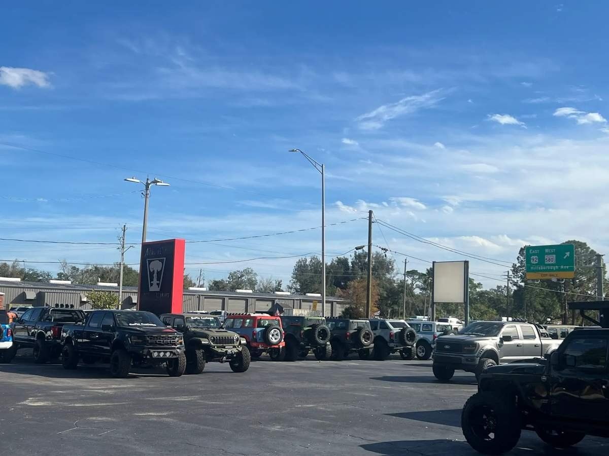 Parking lot full of motorcycles under a blue sky, with signs and traffic lights in the background.