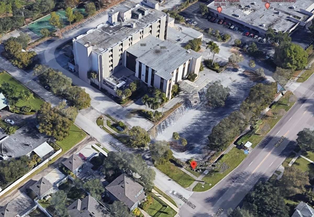 Aerial view of a large apartment complex surrounded by streets, trees, and neighboring houses.