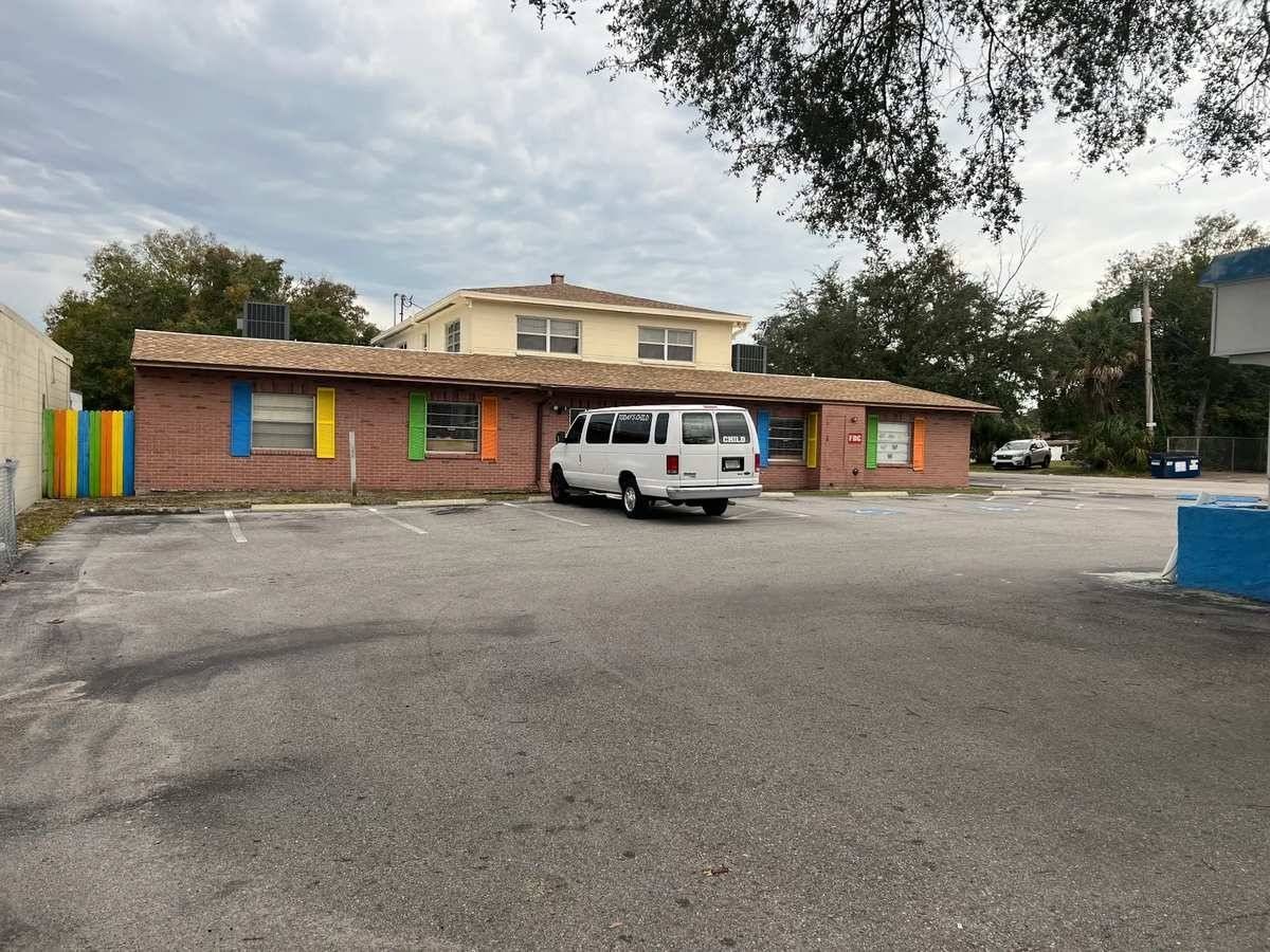 Single-story brick building with a white van parked in front and an empty paved lot