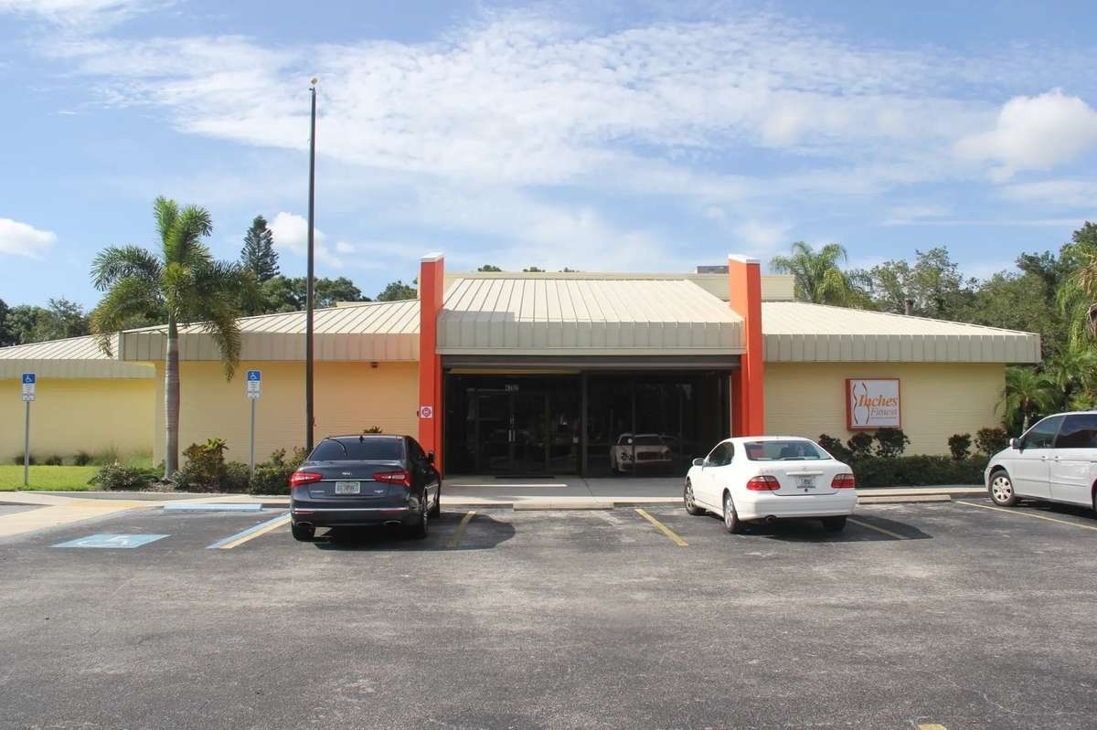 Single-story building with orange columns and parked cars in front under a blue sky.