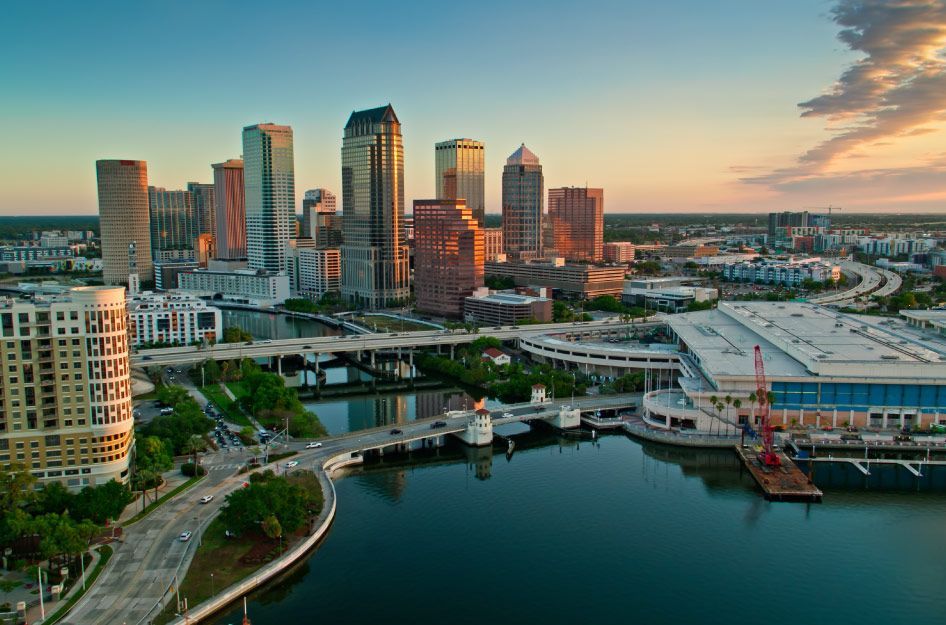 Aerial view of the Tampa, Florida, skyline and Hillsborough River at sunset, featuring modern high-rise buildings.