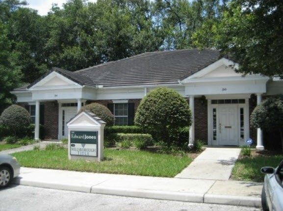 Single-story office building with a sign in front, surrounded by trees and shrubs