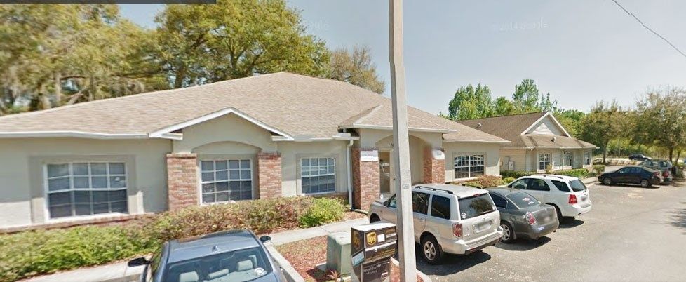 Single-story apartment building with parked cars and a utility truck in front