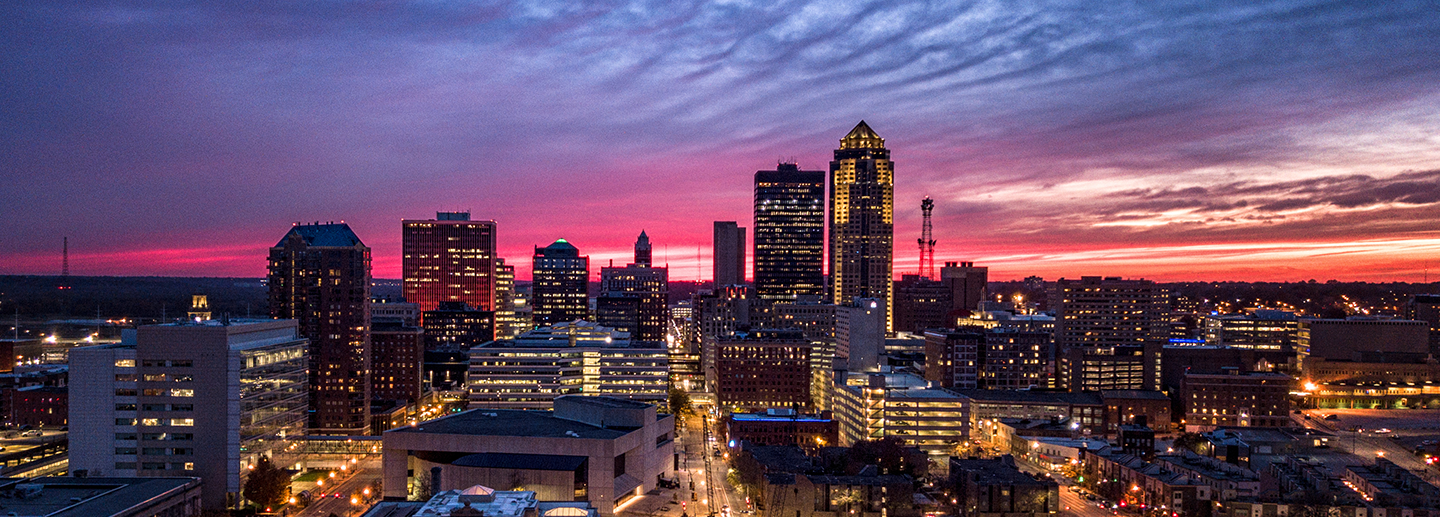 City skyline at sunset with pink and purple sky, buildings lit up, and roads with lights.