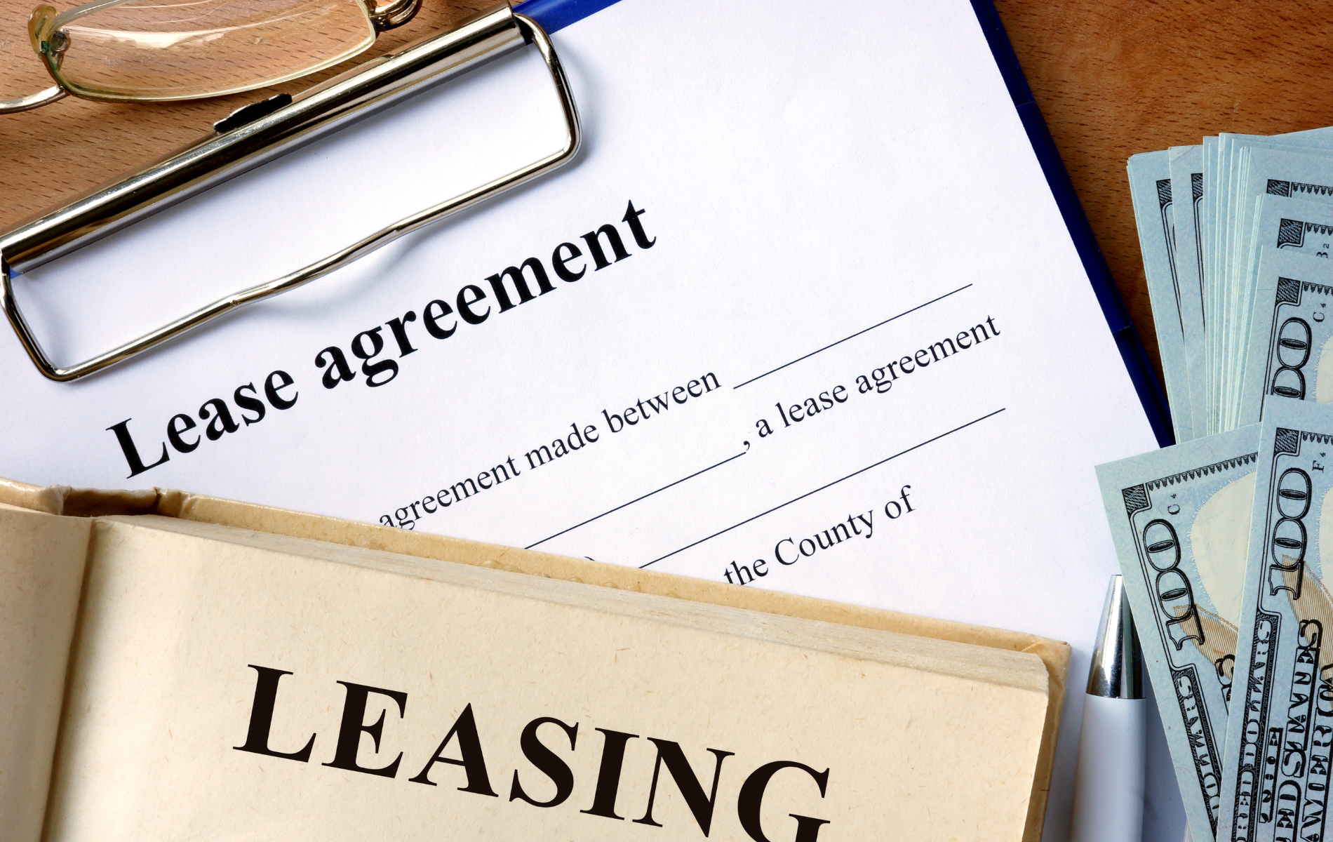 Lease agreement document on clipboard with glasses, cash, and a book labeled