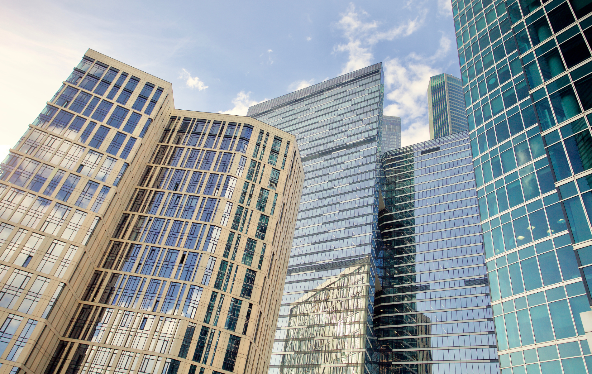 Skyscrapers with glass facades reflect the sky, standing tall under a partly cloudy sky.