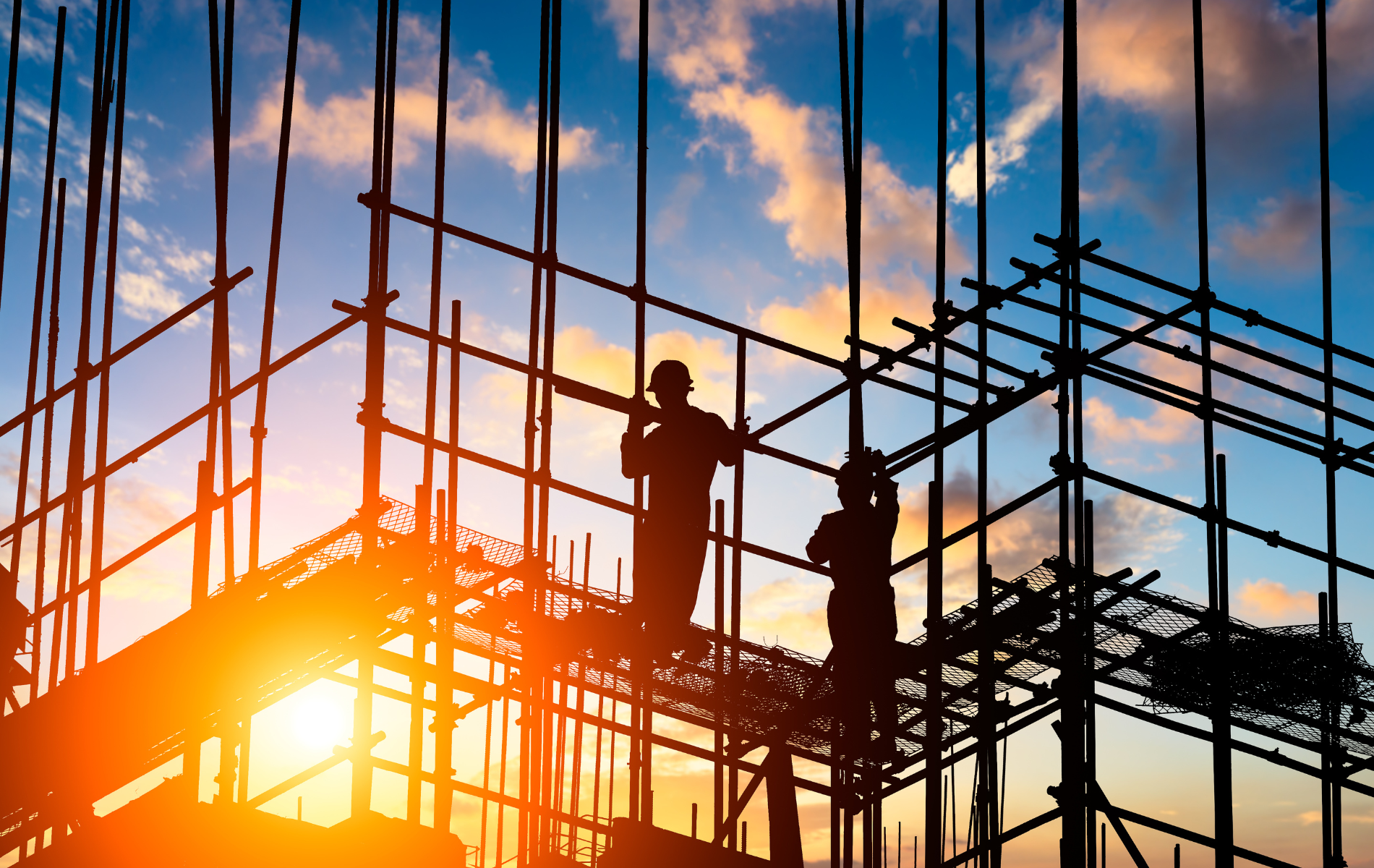 Construction workers on scaffolding at sunset. Silhouette of workers, orange glow.