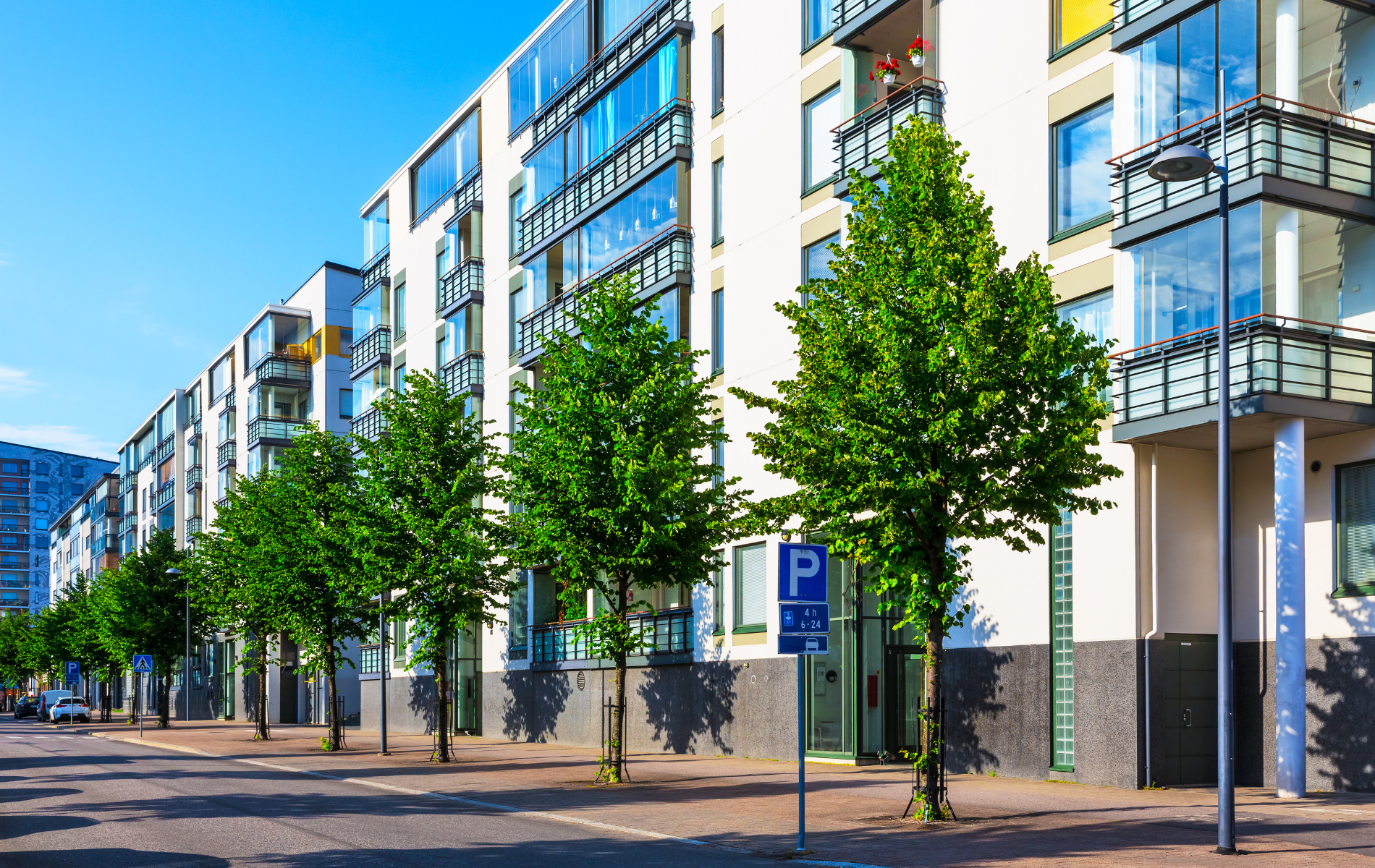 Row of modern apartment buildings with green trees on the sidewalk, sunny day.