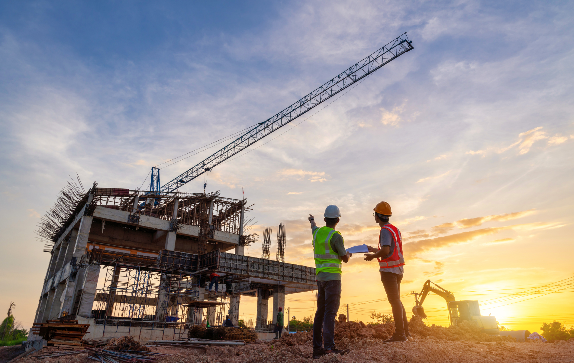 Construction workers on a building site, crane overhead, pointing at structure during sunset.