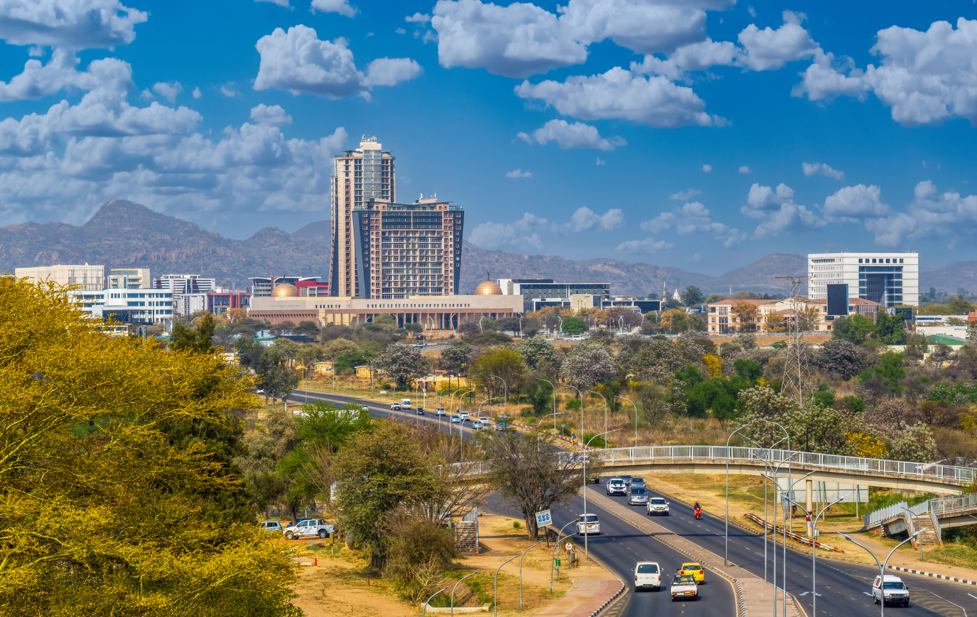 Cityscape with modern buildings, highway, and blue sky with clouds.