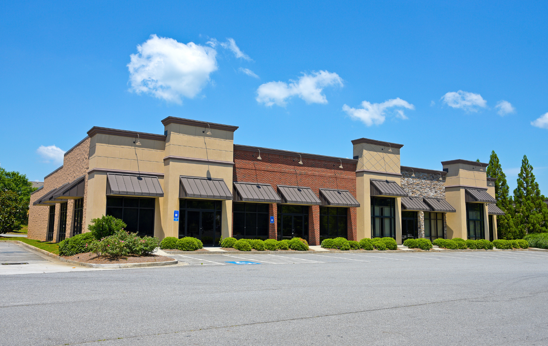 Empty commercial building with dark windows and awnings, beige and brick exterior, blue sky.