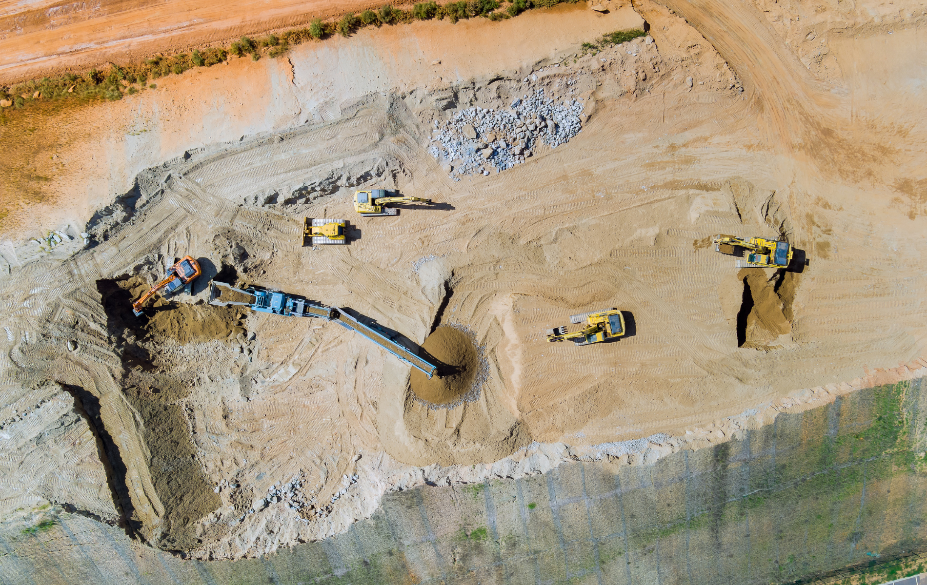 Aerial view of a construction site with several yellow bulldozers and machinery working on a dirt pile.