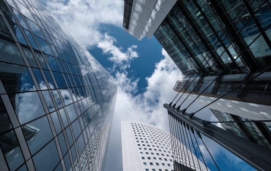 Skyscrapers reaching towards a blue sky with fluffy white clouds, viewed from below.