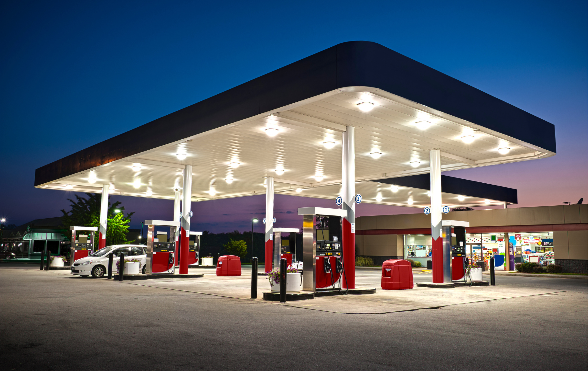 Gas station at dusk with illuminated canopy, pumps, and a car.