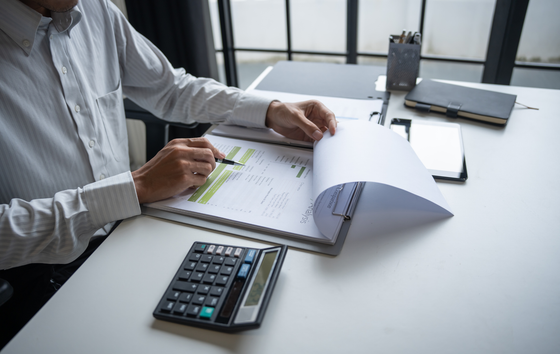 Person reviewing documents at a desk, with a calculator and tablet nearby.