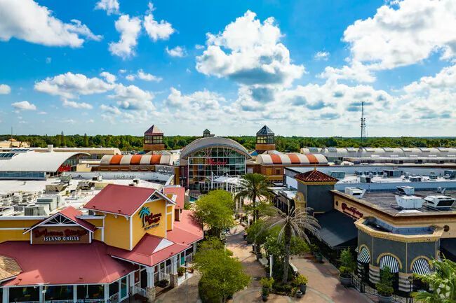 Aerial view of a shopping mall with colorful buildings, palm trees, and a blue sky with clouds.