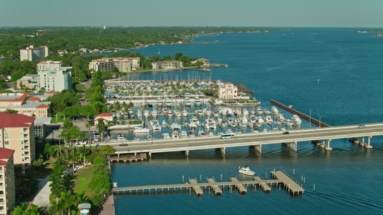 Aerial view of Sarasota Bay, Florida, with a bridge, marina filled with boats, and buildings along the waterfront.