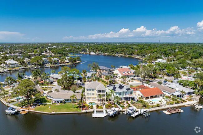 Aerial view of waterfront homes on a lake, boats docked at piers, blue water, green trees, and a clear sky.