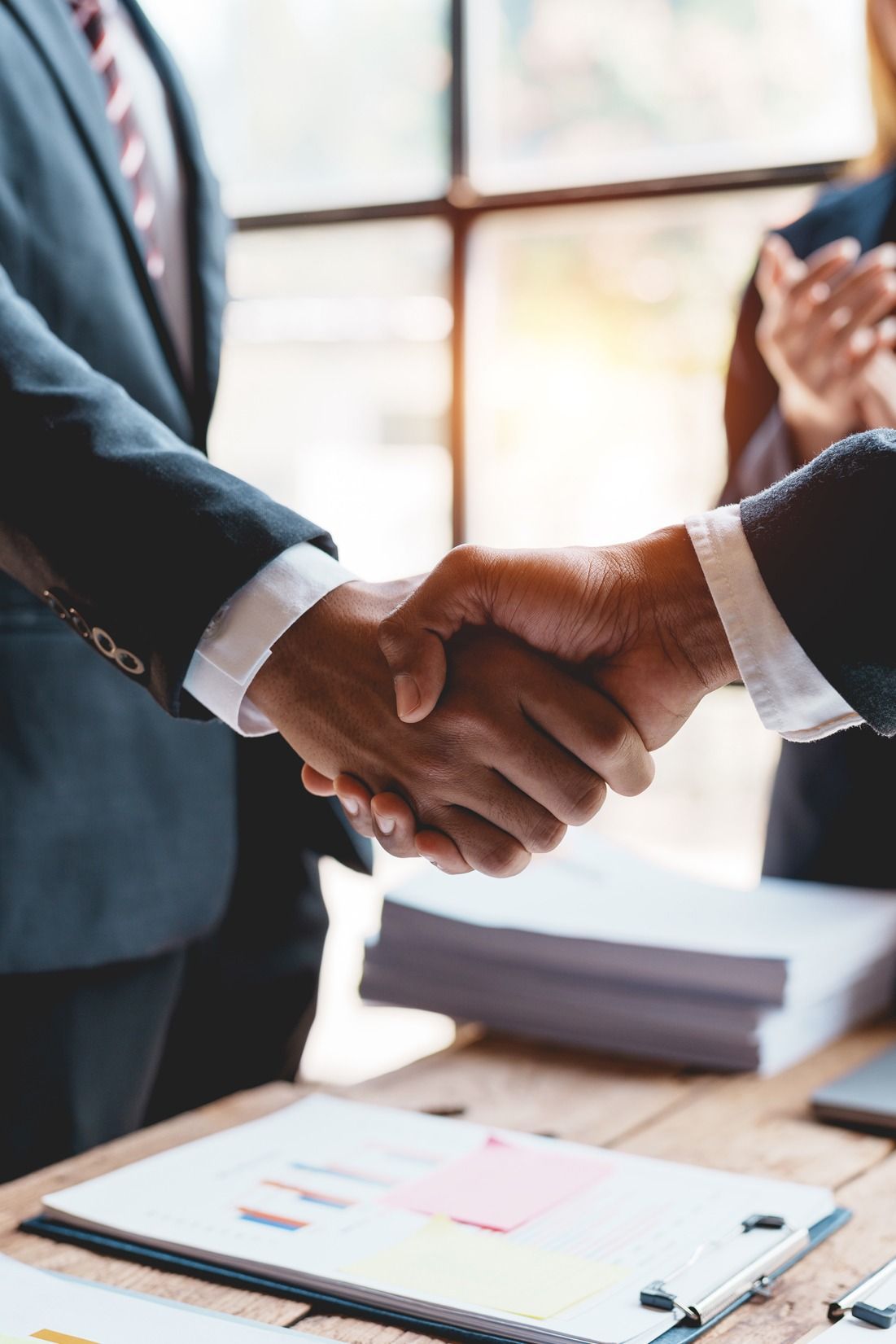 Businesspeople shaking hands over a desk with documents and a pen in a bright office