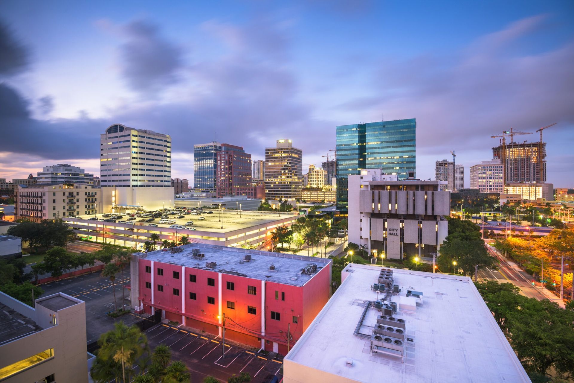 Downtown city skyline at dusk with illuminated buildings and a cloudy purple sky