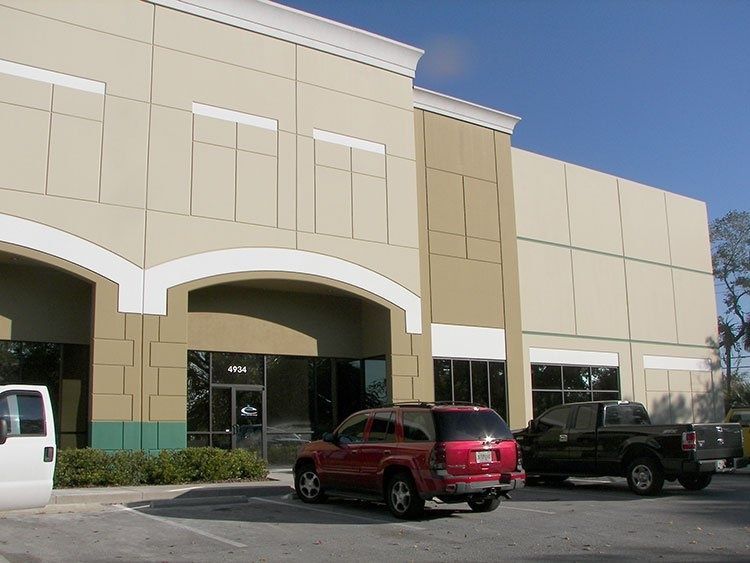 Storefront with tan facade and arched entry, with red and black SUVs parked in front.