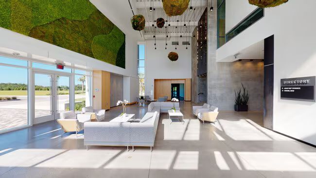 Modern lobby with gray sofas, a moss wall, and large windows.